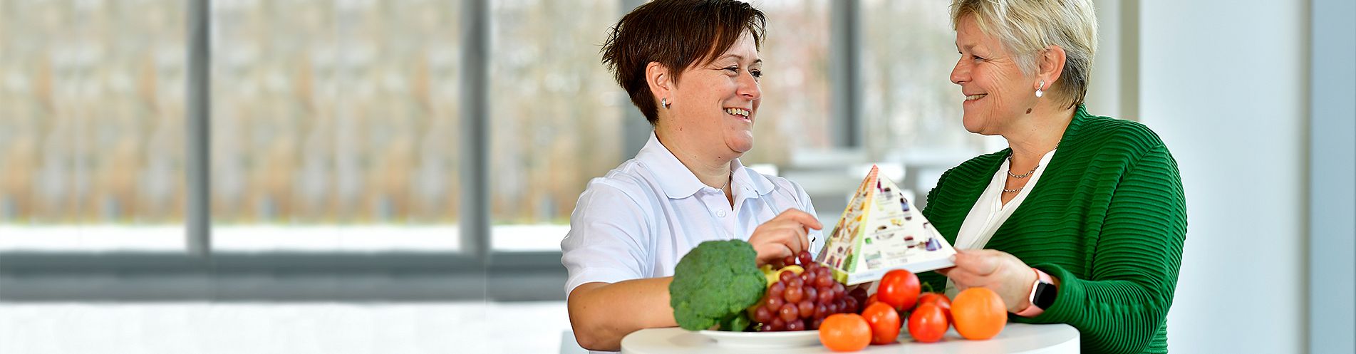 Bild: Eine Mitarbeiterin der Gastronomie erklärt einer Patientin die Ernährungspyramide